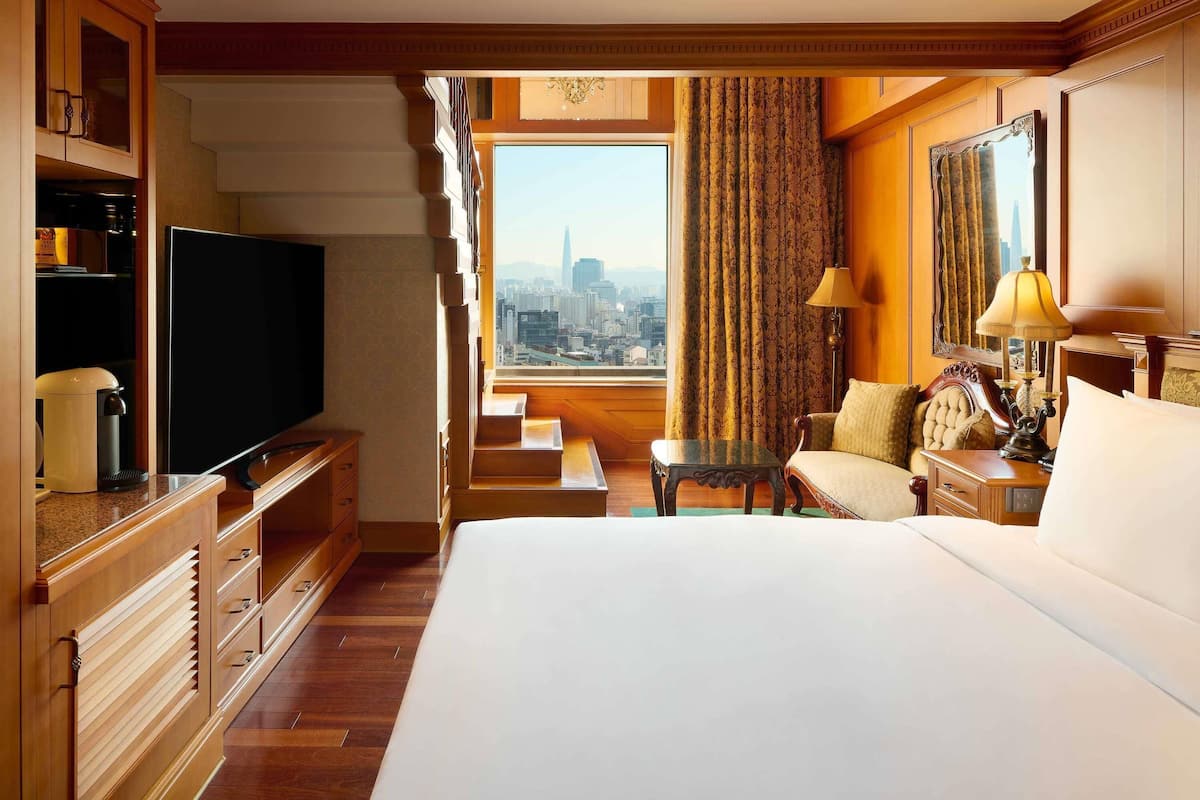 A hotel room with a bed, a television, a coffee maker, a table, and a view of a cityscape.