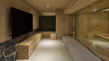A modern bathroom with a stone wall, wooden benches, and a glass partition.