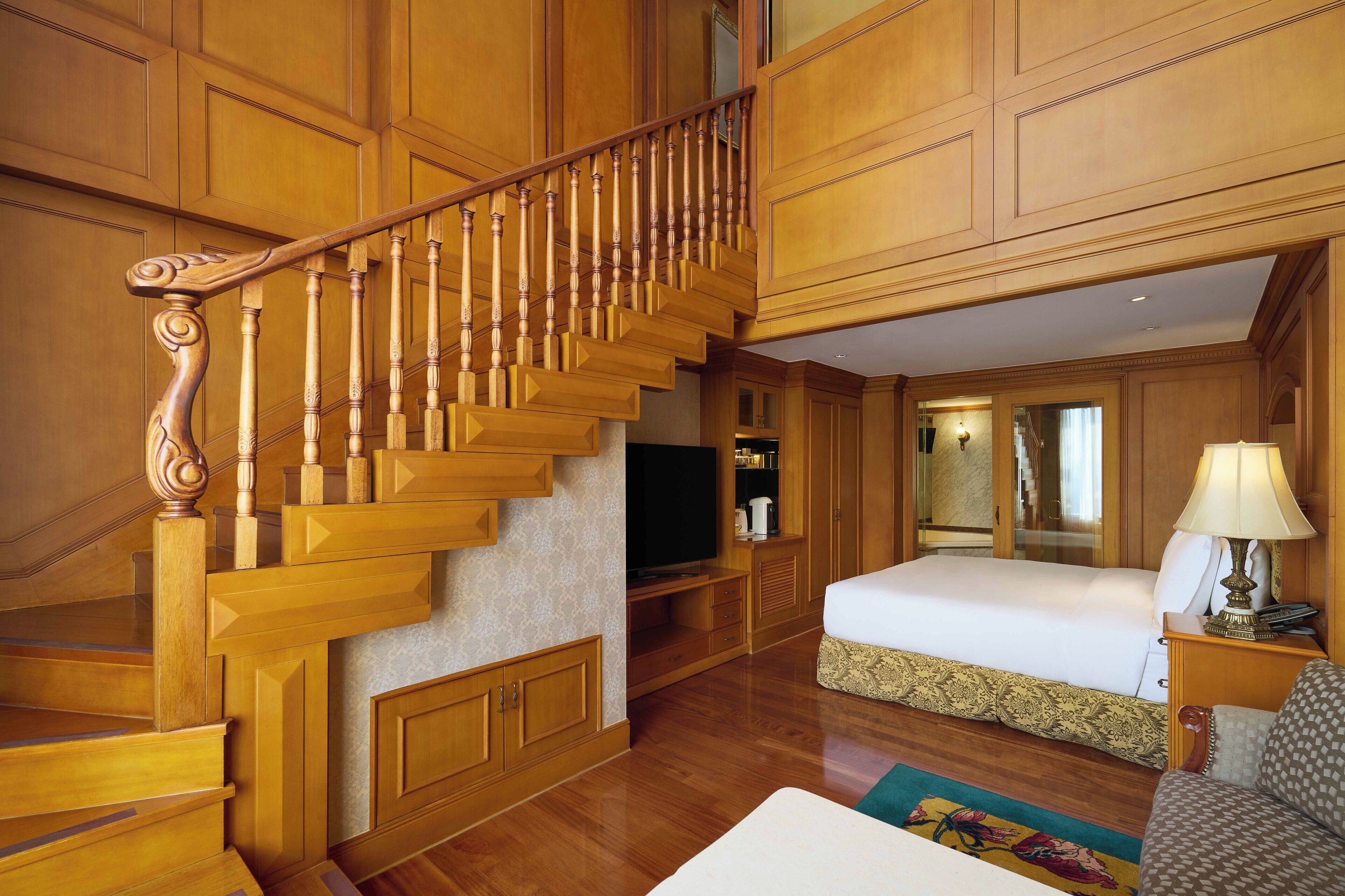 Una habitación de hotel con una escalera de madera, una cama, un televisor y un baño con un espejo.