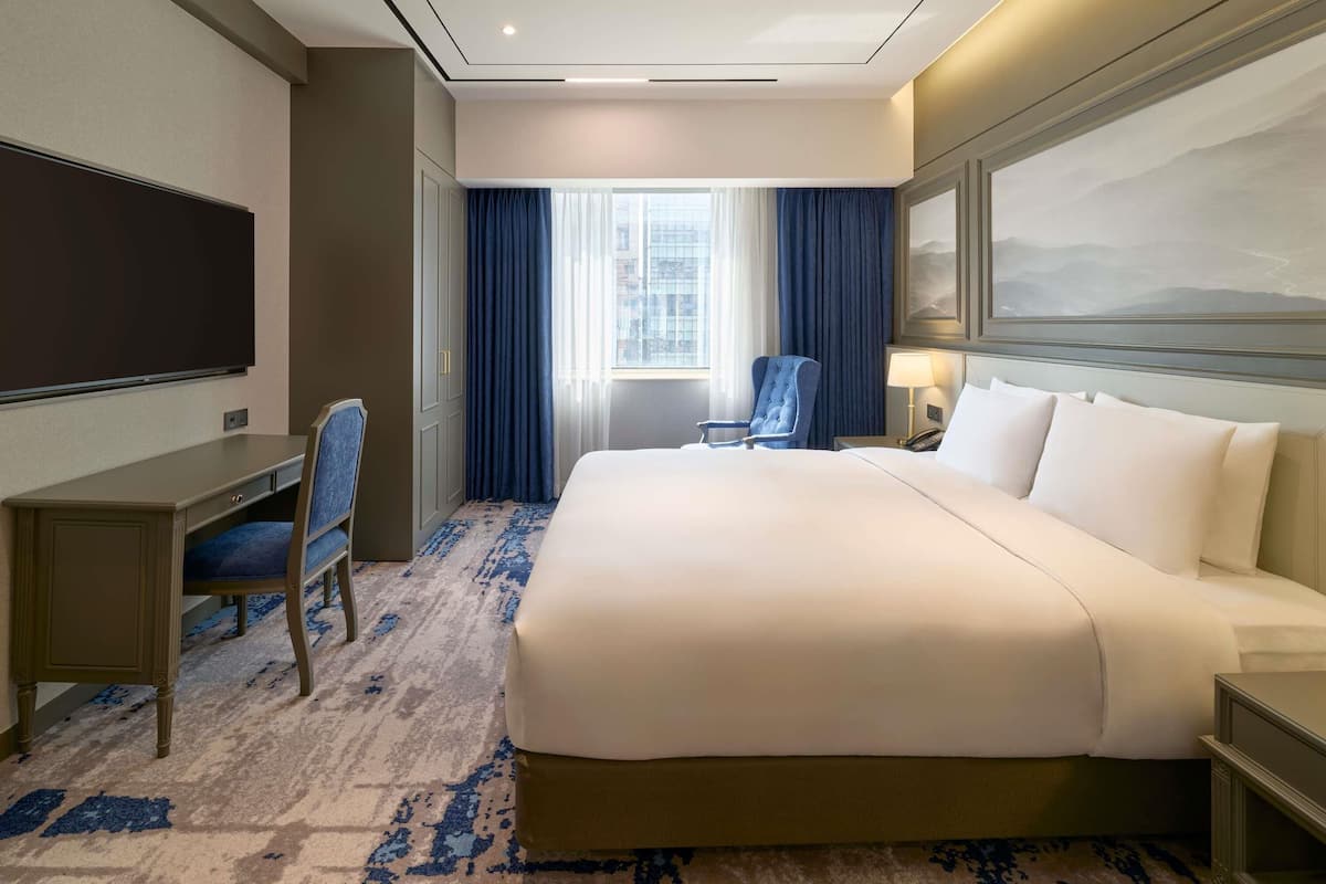 Una habitación de hotel con una cama grande, un escritorio, una silla, un televisor y una ventana con cortinas.