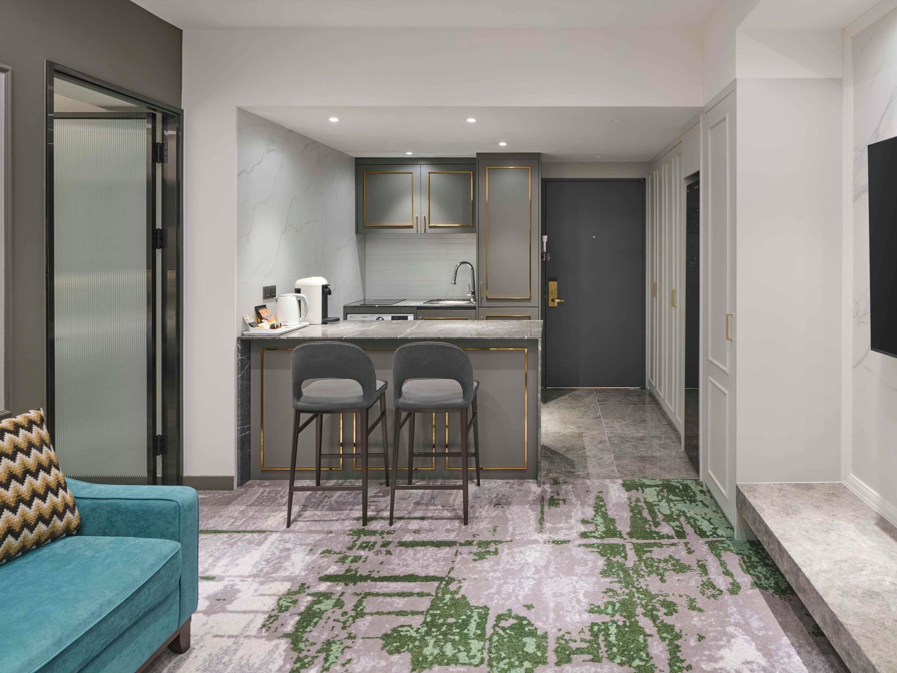 Una cocina compacta con una isla central, dos taburetes de bar, un sofá y una alfombra estampada.