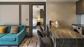 Quarto de hotel moderno com sofá verde-água, ilha de cozinha em mármore e máquina de lavar roupa.