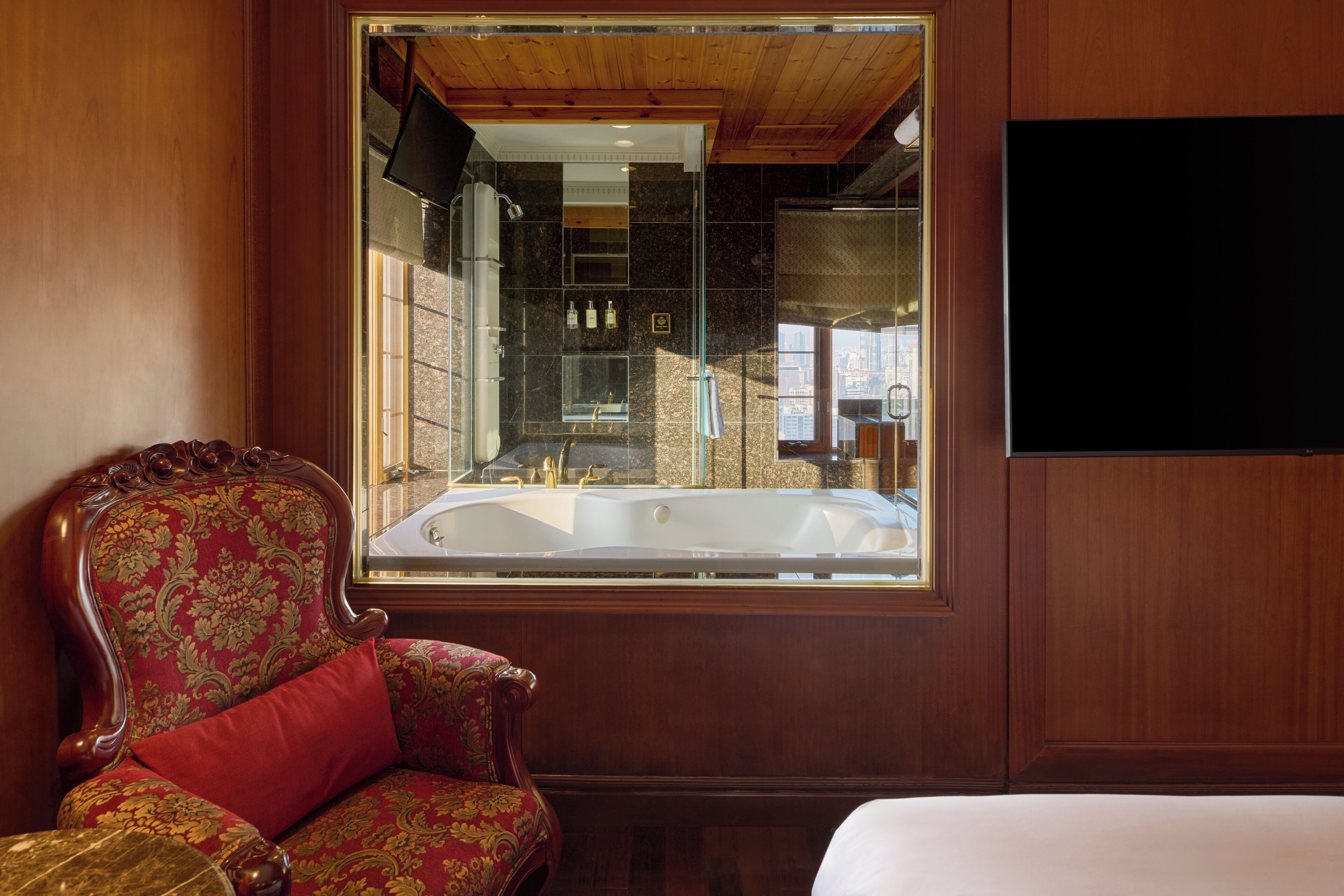A room with a large window, a wooden chair, a bed, and a bathtub.