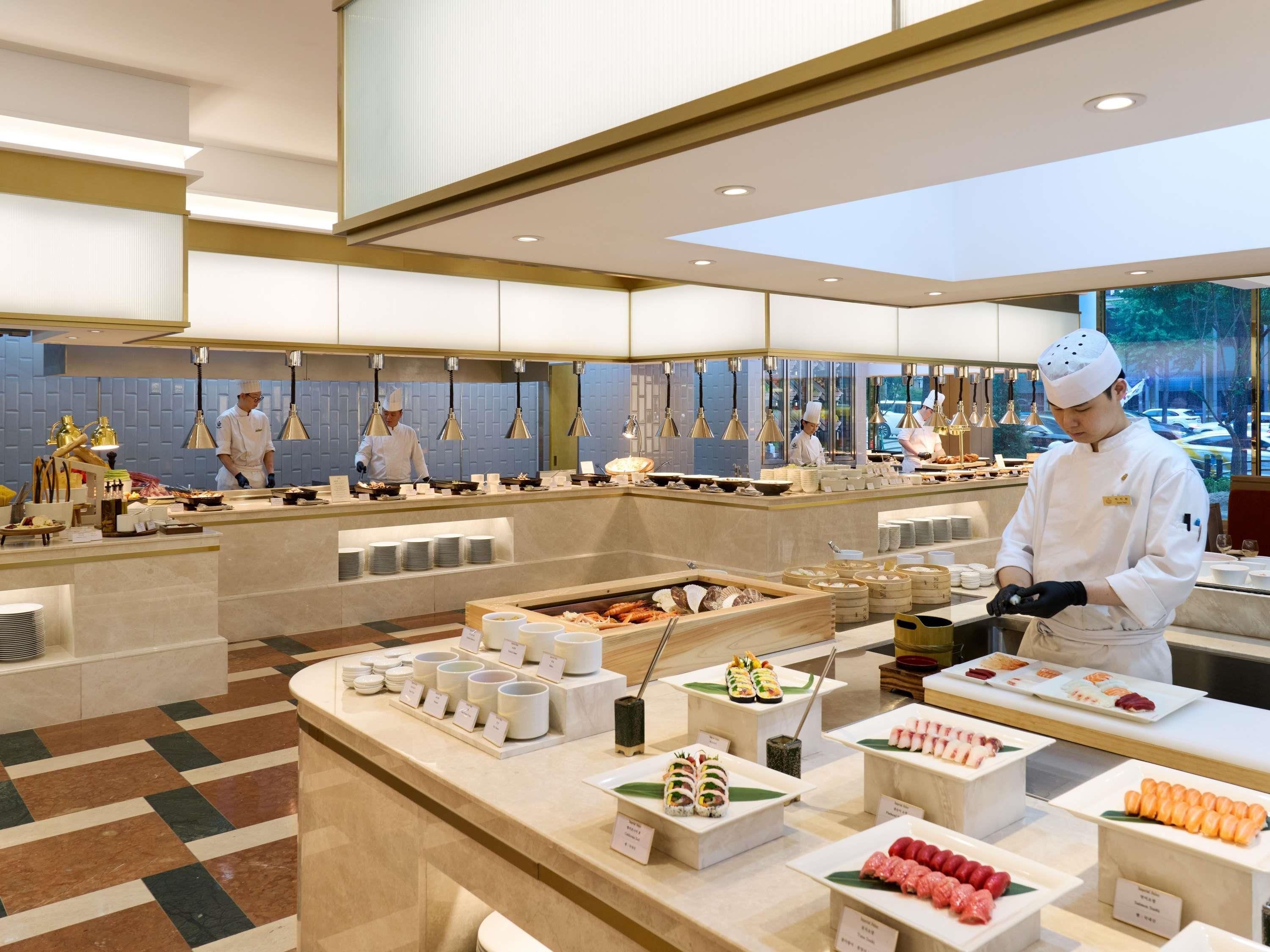 Una cocina moderna con chefs preparando alimentos, un bufé con diversos platos y un suelo a cuadros.