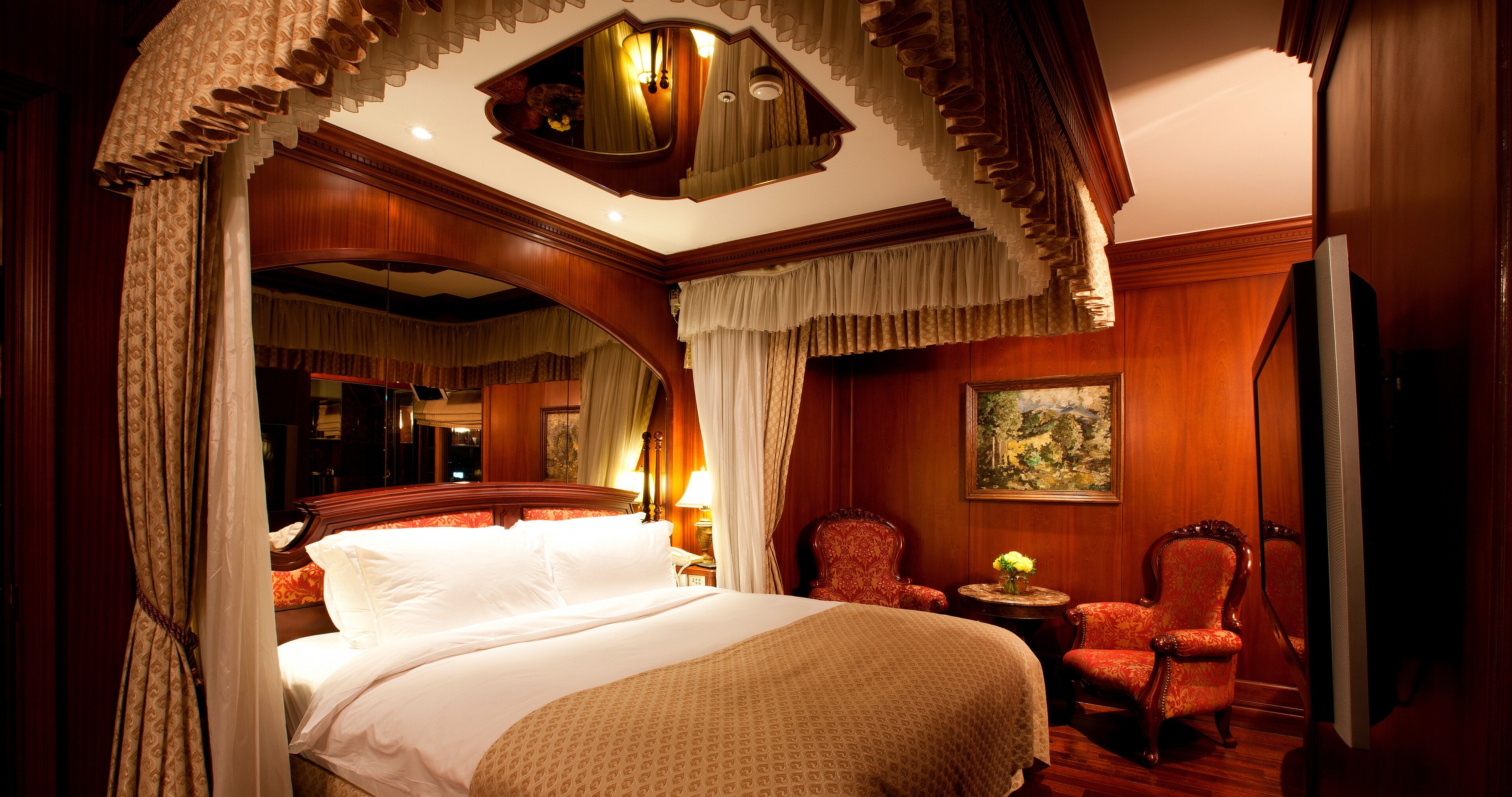 Un dormitorio lujoso con una cama grande, cortinas ornamentales, un candelabro y un cuadro en la pared.