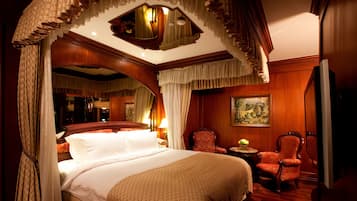 A luxurious bedroom with a large bed, ornate curtains, a chandelier, and a painting on the wall.