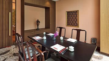Une salle de conférence avec une longue table, des chaises, un vase de fleurs et un élément décoratif mural.