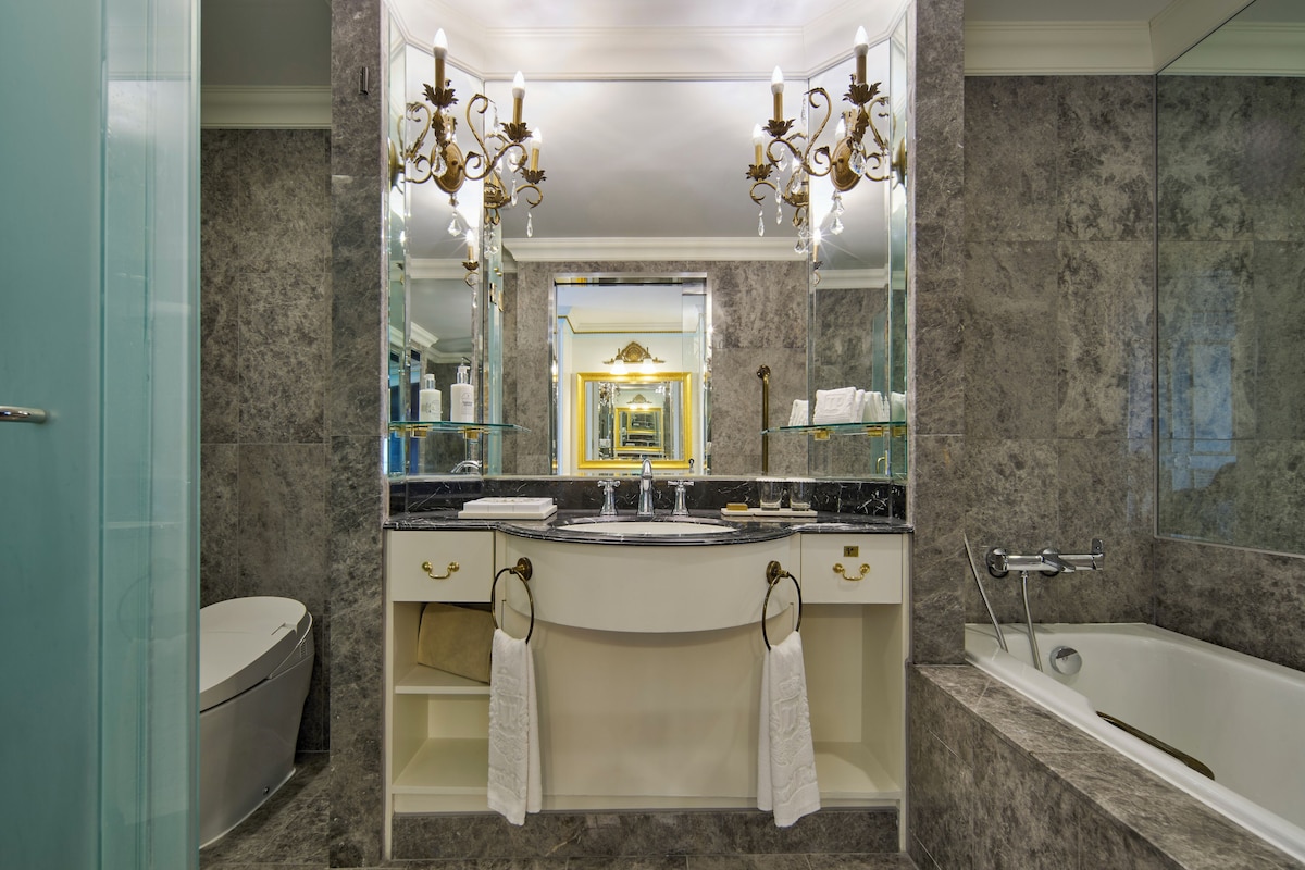 A bathroom with a marble sink, a bathtub, and a large mirror.