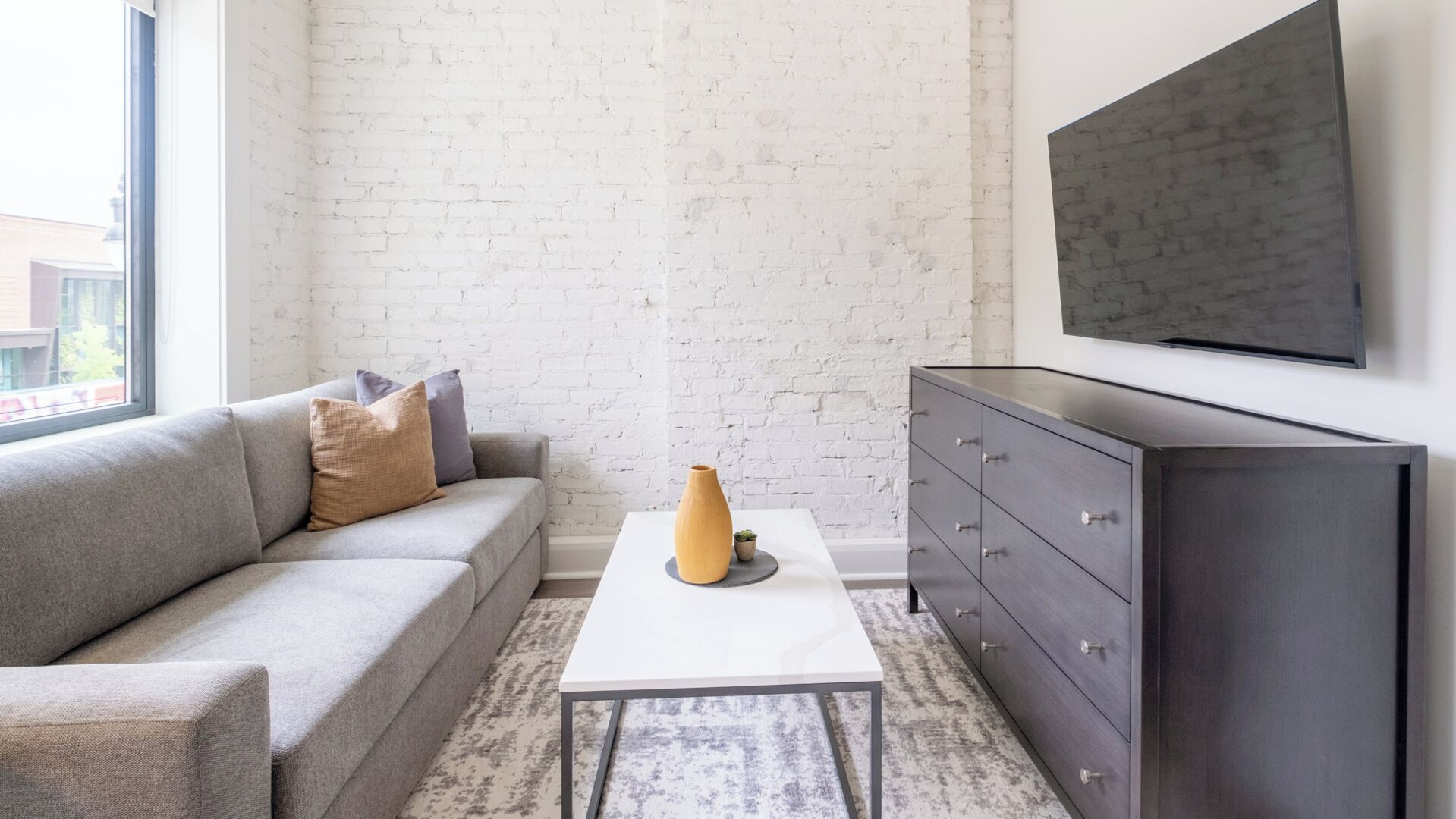 Una sala moderna con un sofá gris, una mesa de centro blanca y un aparador de madera oscura.