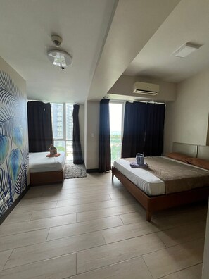 A modern hotel room with a bed, a sofa, and a large window with curtains. - Condominium Rentals at Mactan Newtown (Lapu-Lapu)