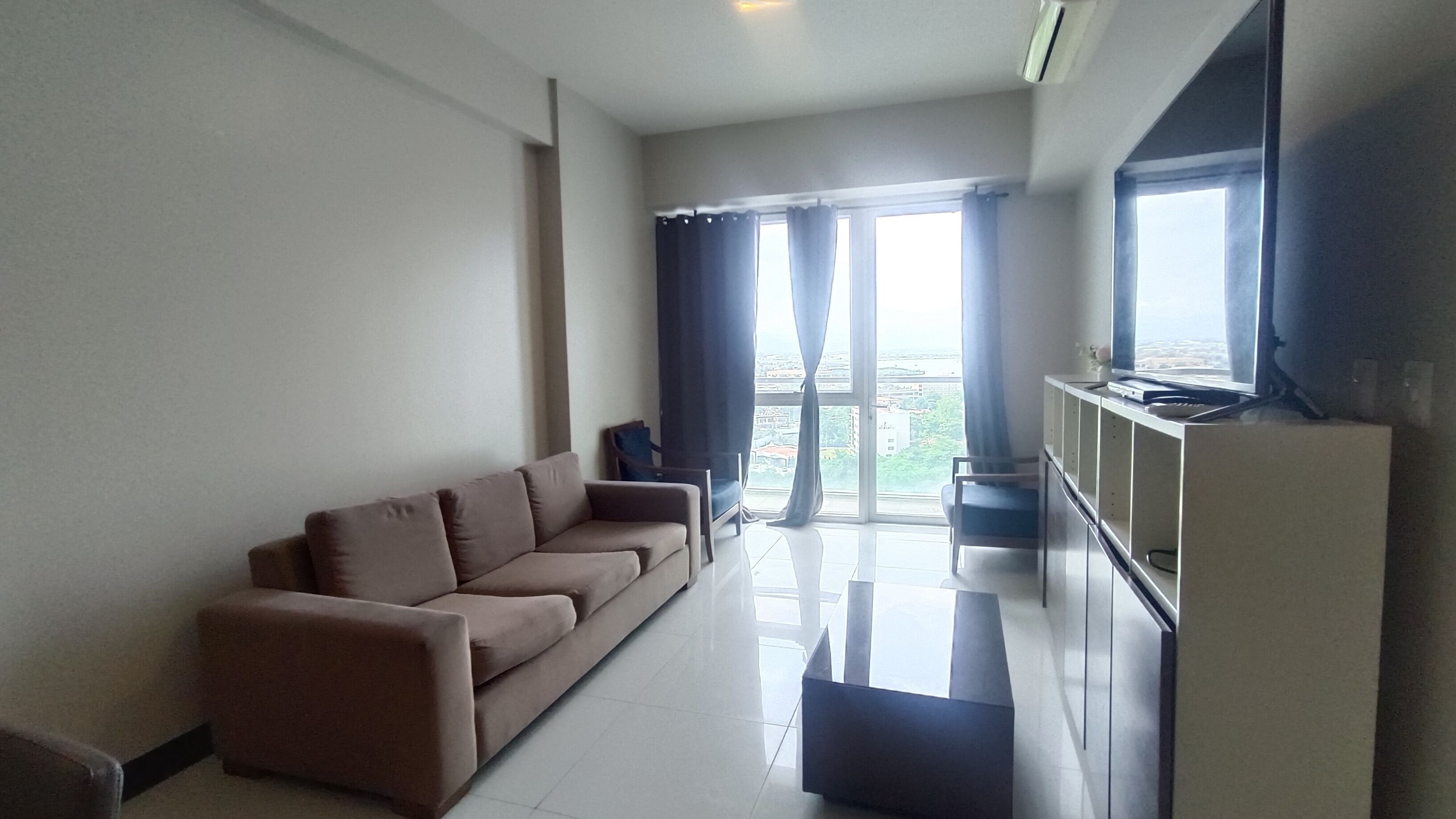 A modern living room with a sofa, a flat-screen TV, and a sliding glass door leading to a balcony.