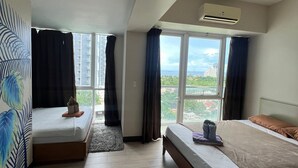 Hotellihuone, jossa on kaksi sänkyä, suuri ikkuna ja ilmastointilaite.