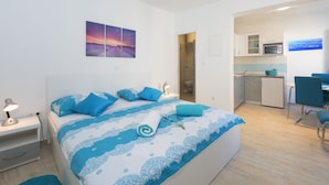 A bedroom with a bed, a nightstand, a desk, and a chair. There is a bathroom visible through an open door. - Apartments Nona 2 (Hvar)