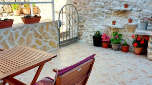 A patio with a wooden table and chairs, potted plants, a stone wall, and a metal gate. - Apartments Nona 2 (Hvar)