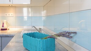 A modern kitchen with white cabinets, a sink, and a teal basket with lavender flowers. - Apartments Nona 2 (Hvar)