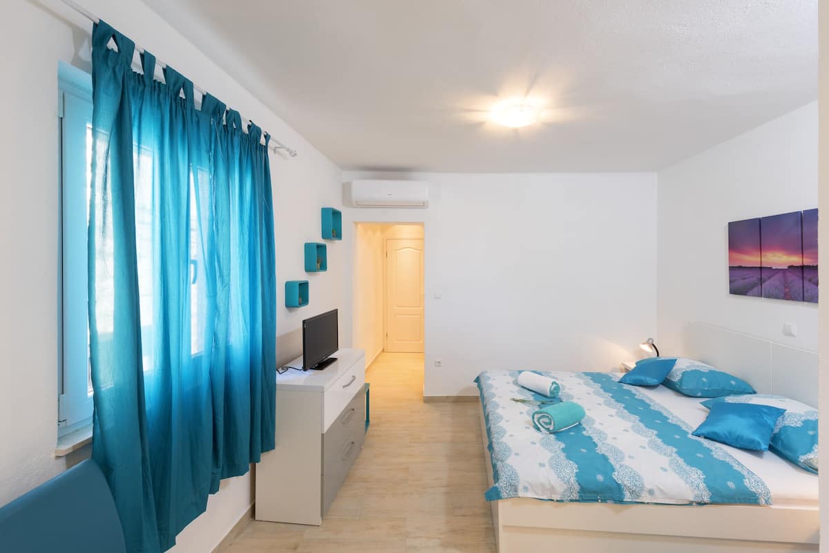 Une chambre à coucher comprenant un lit, un bureau, une télévision et une porte donnant sur une autre pièce.