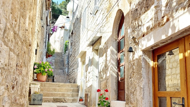 A narrow stone alleyway with steps leading to a building with a wooden door. - Apartments Nona 2 (Hvar)