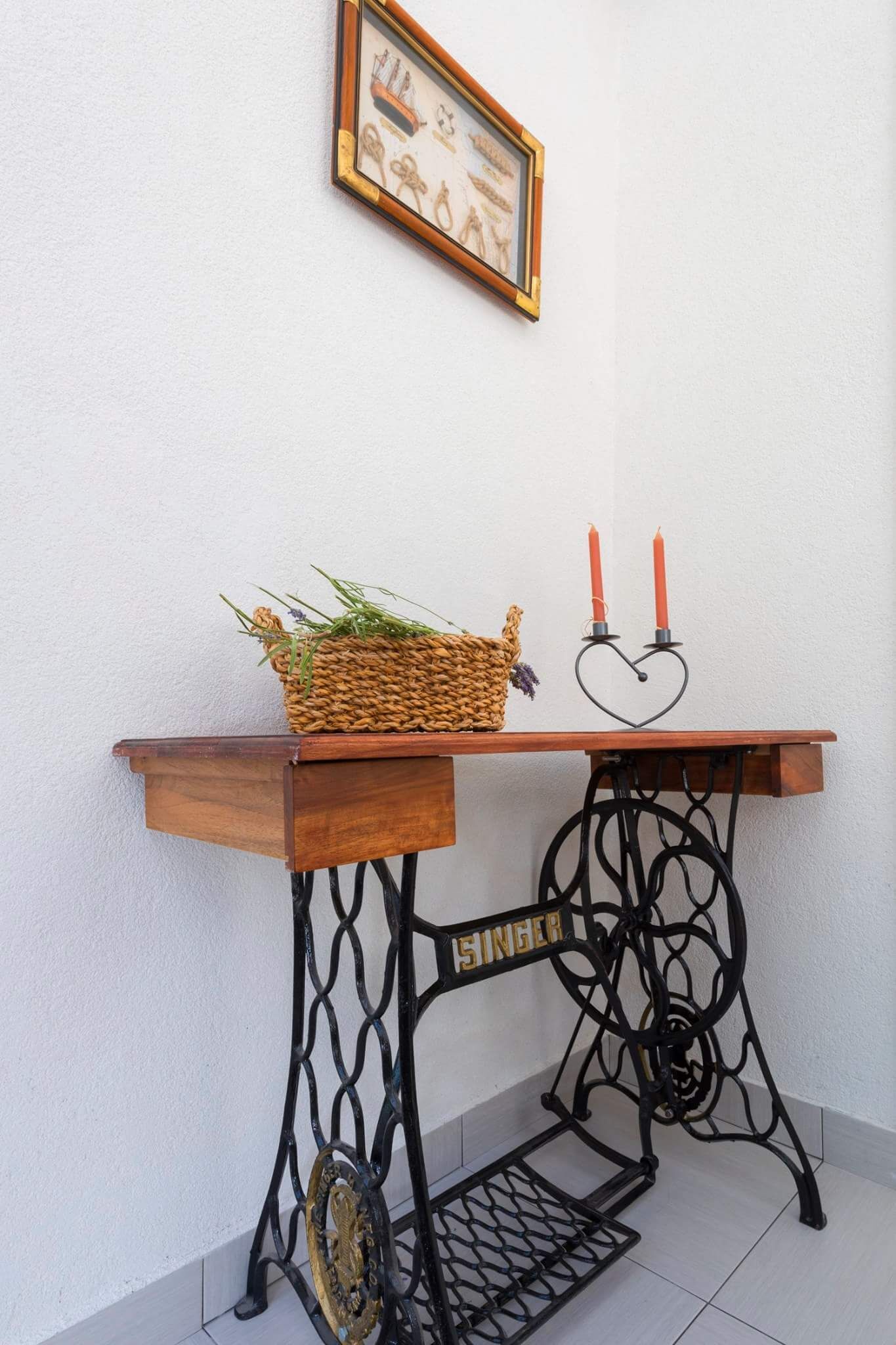 Una mesa de madera con una cesta trenzada y dos velas rojas sobre soportes con forma de corazón.