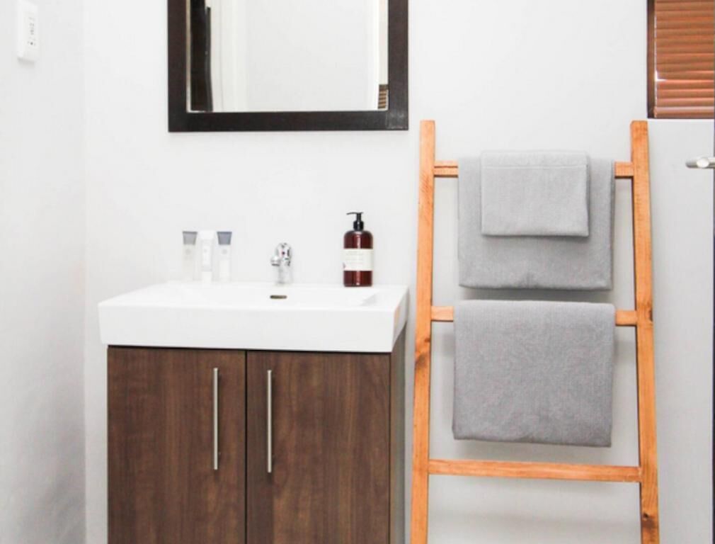 A bathroom with a white sink, dark wooden cabinets, a mirror, and a wooden ladder with two towels.