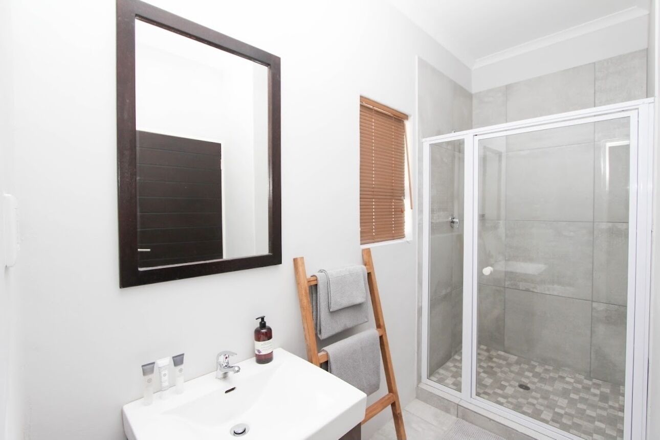 A bathroom with a white sink, a mirror, a wooden ladder, and a glass-enclosed shower.