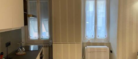 A compact kitchen with a built-in refrigerator, a window with blinds, and a radiator.