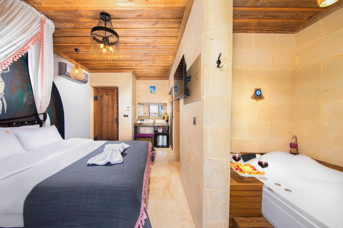 A hotel room with a bed, a small kitchenette, a bathtub, and a shower.