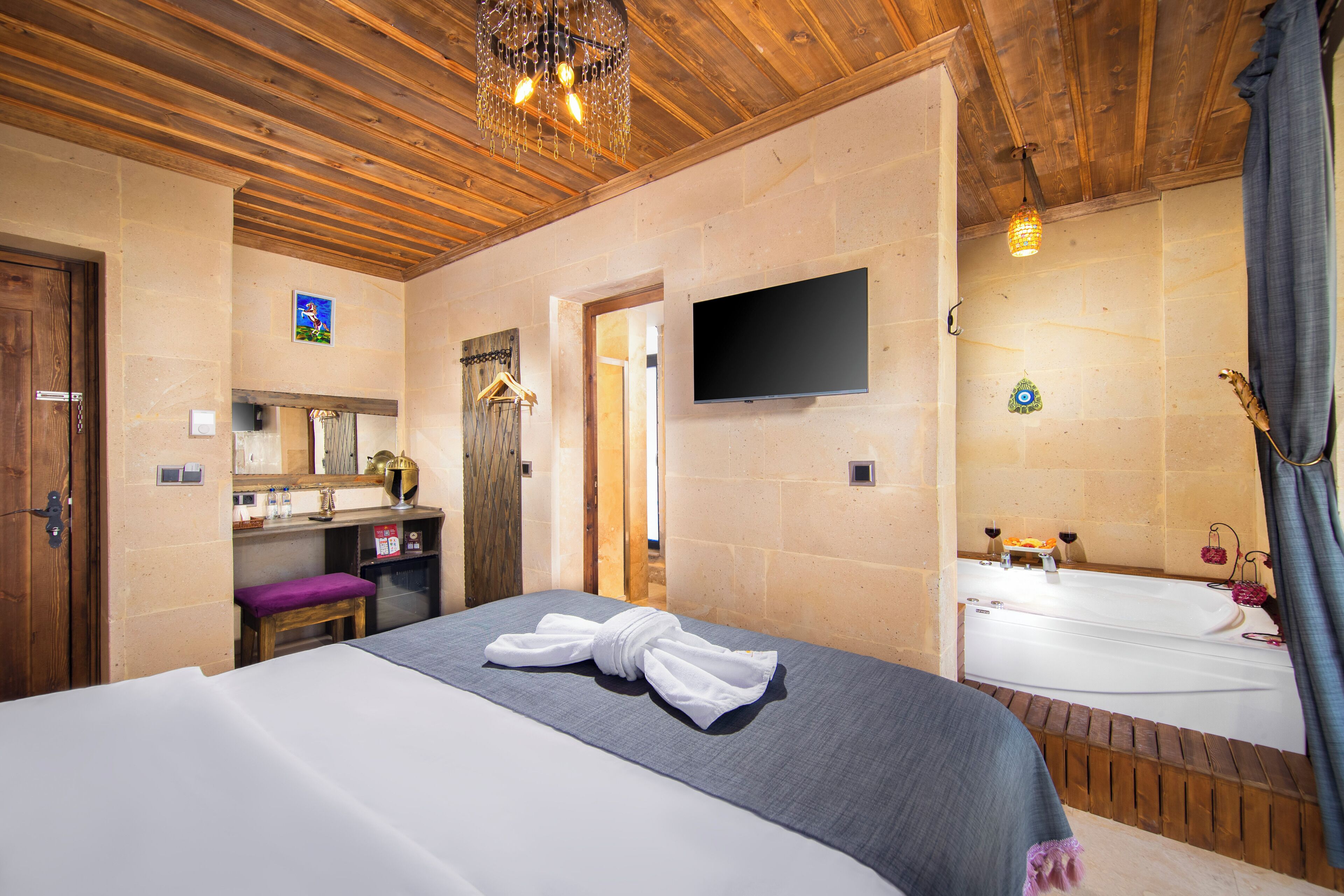 Habitación de hotel con techo de madera, cama con ropa blanca, televisor montado en la pared y una bañera.