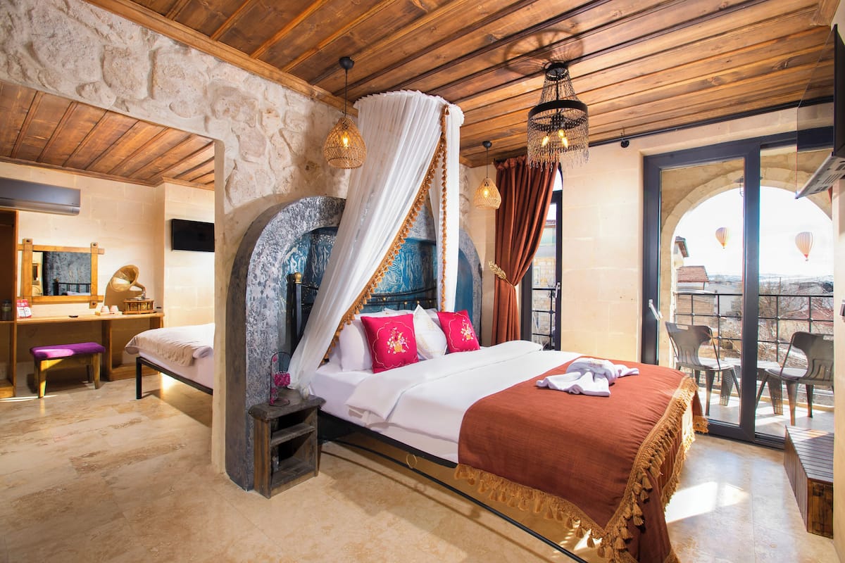 A bedroom with a large bed, a desk, and a balcony with chairs.
