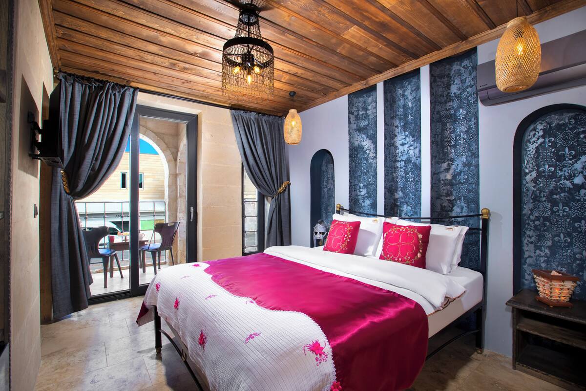 A bedroom with a bed, curtains, a chandelier, and a view of the outside.