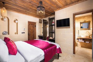 A bedroom with a bed, wooden ceiling, a chandelier, a TV, and a bathroom with a sink and mirror.