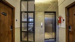 A hotel lobby with a wooden door labeled "202", a glass elevator door, and a fire extinguisher mounted on the wall. - StayBird Divine Suites Business Hotel (Pune)