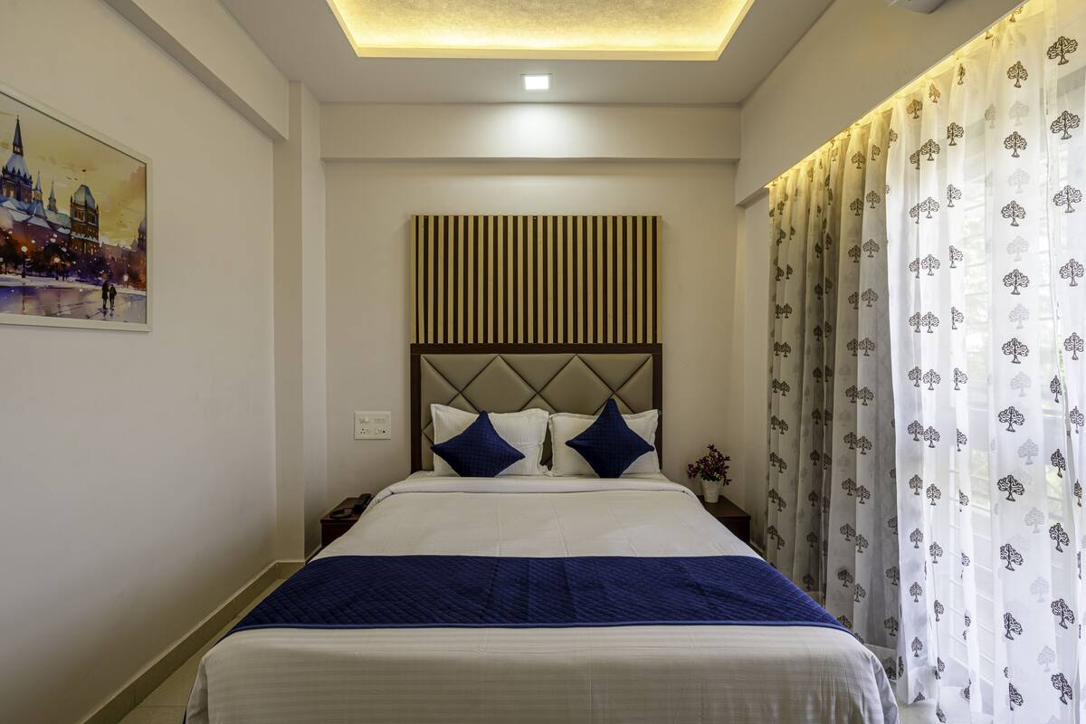 A hotel room with a bed, a headboard, a painting on the wall, and curtains.