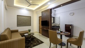 A modern living room with a sofa, chairs, a coffee table, a TV, and a refrigerator. - StayBird Divine Suites Business Hotel (Pune)