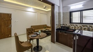A modern kitchen with a dining area, featuring a round table, chairs, a sofa, and built-in appliances. - StayBird Divine Suites Business Hotel (Pune)