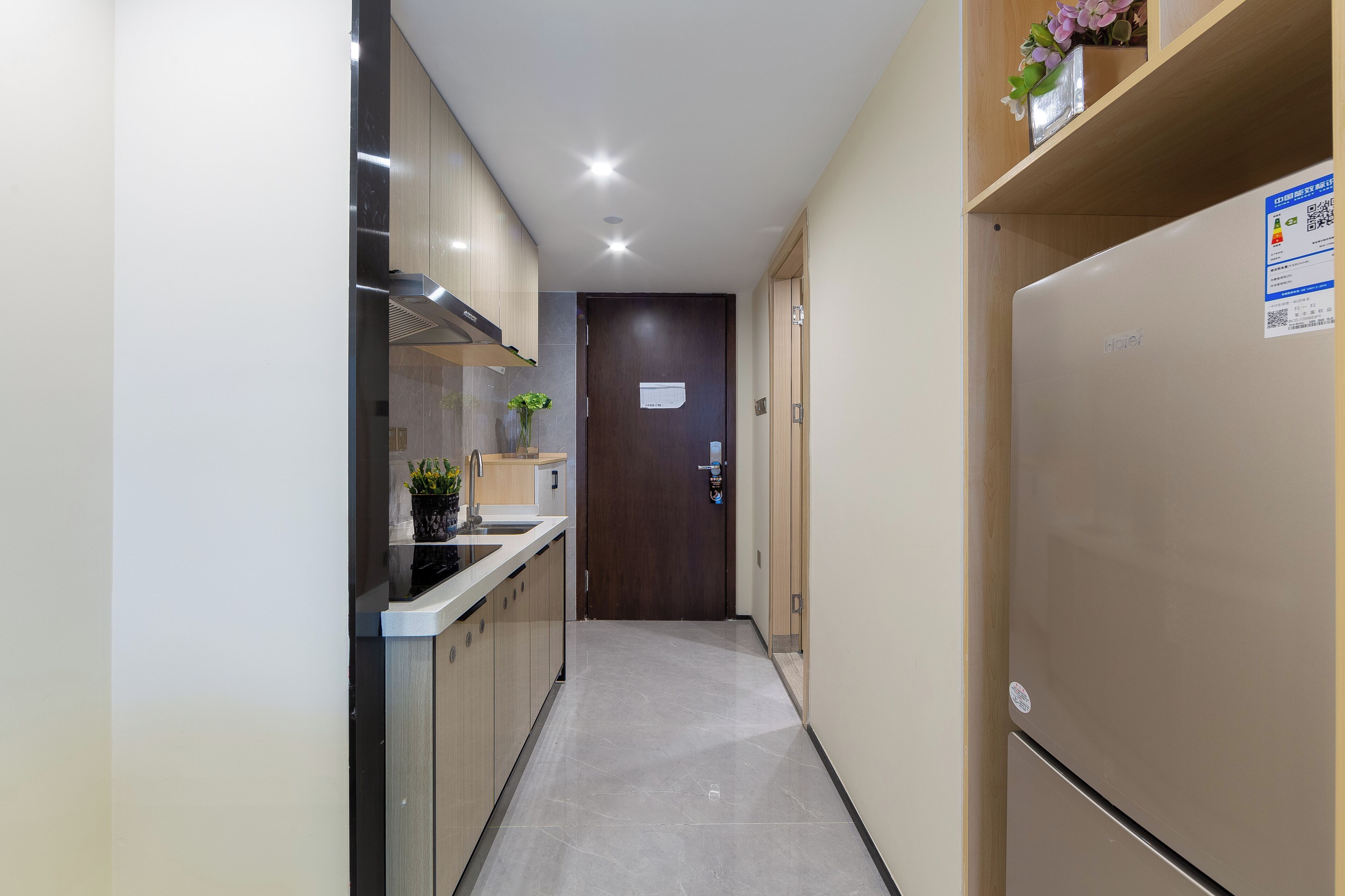 A narrow hallway with a kitchen area on one side, including cabinets, a stove, and a refrigerator.