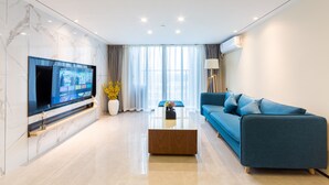 Un salon moderne avec un téléviseur à écran plat, un canapé bleu, une table basse et une grande fenêtre avec des rideaux.