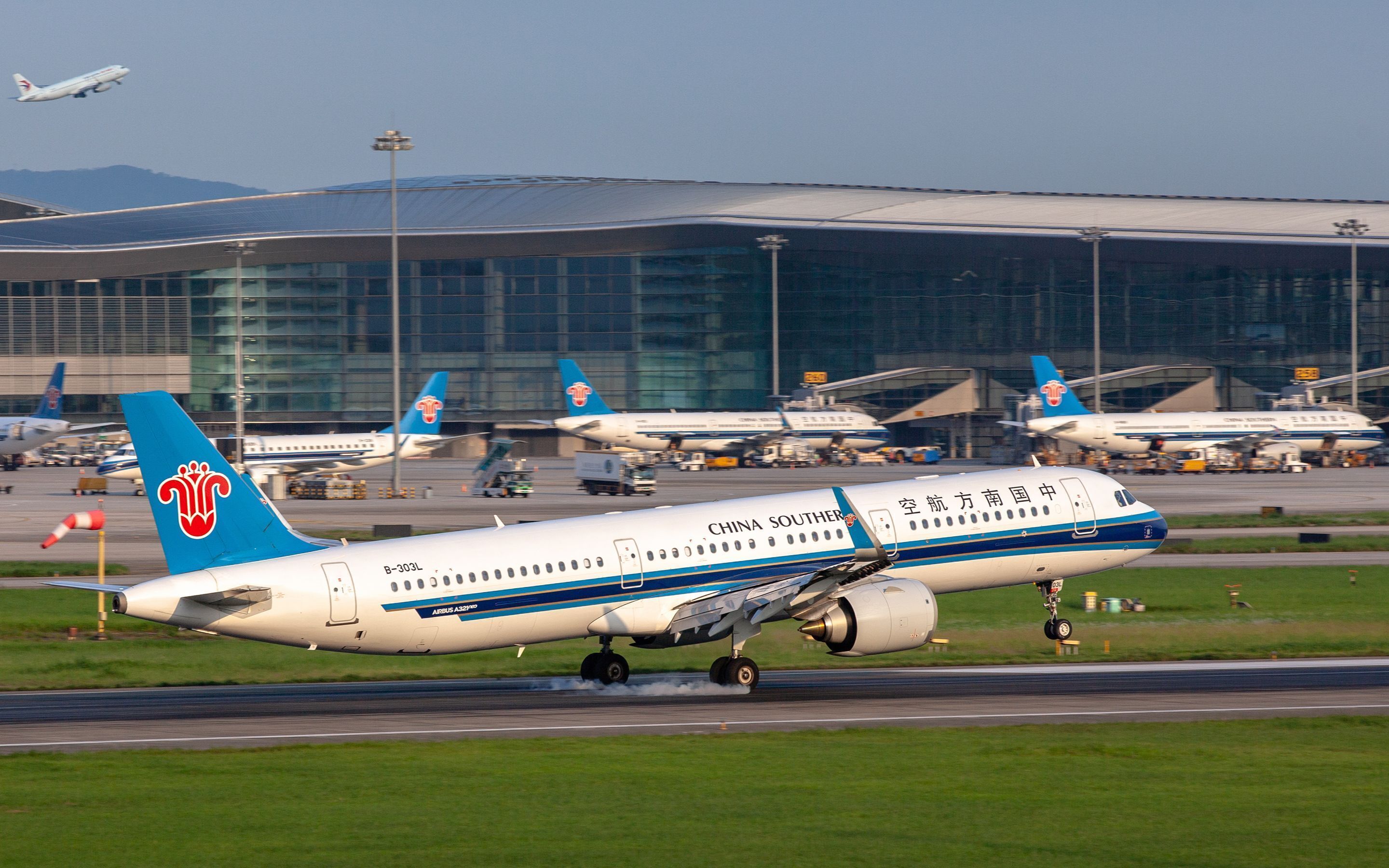 Ein Flughafen mit mehreren Flugzeugen, darunter eine China Southern Airbus A320, die landet.
