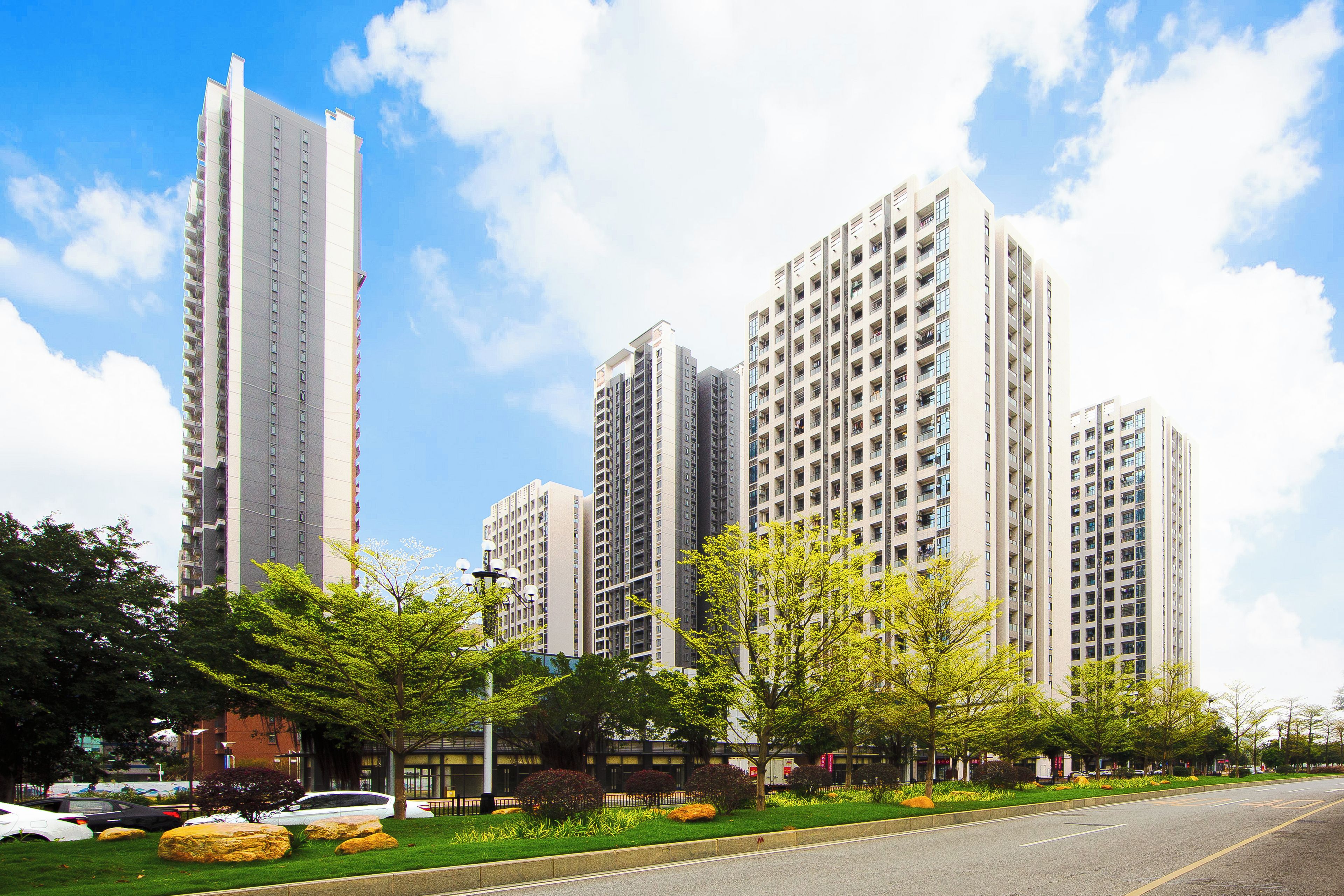A high-rise residential building with multiple floors, surrounded by well-maintained greenery and a clear sky.