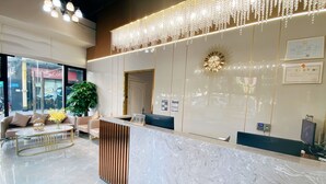 A modern reception area with a marble counter, a large potted plant, and a seating area with sofas and a coffee table.