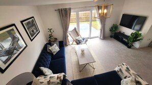 A modern living room with a dark blue sofa, a coffee table, and a TV mounted on the wall. There is a sliding glass door leading to a patio area. - Insch House -  Retreat Group (Kingussie (nr Aviemore))