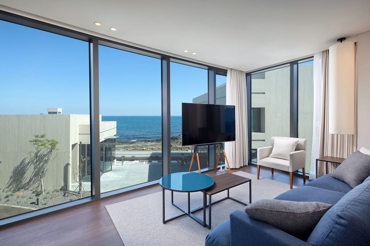 A modern living room with a large TV, comfortable seating, and a view of the ocean.
