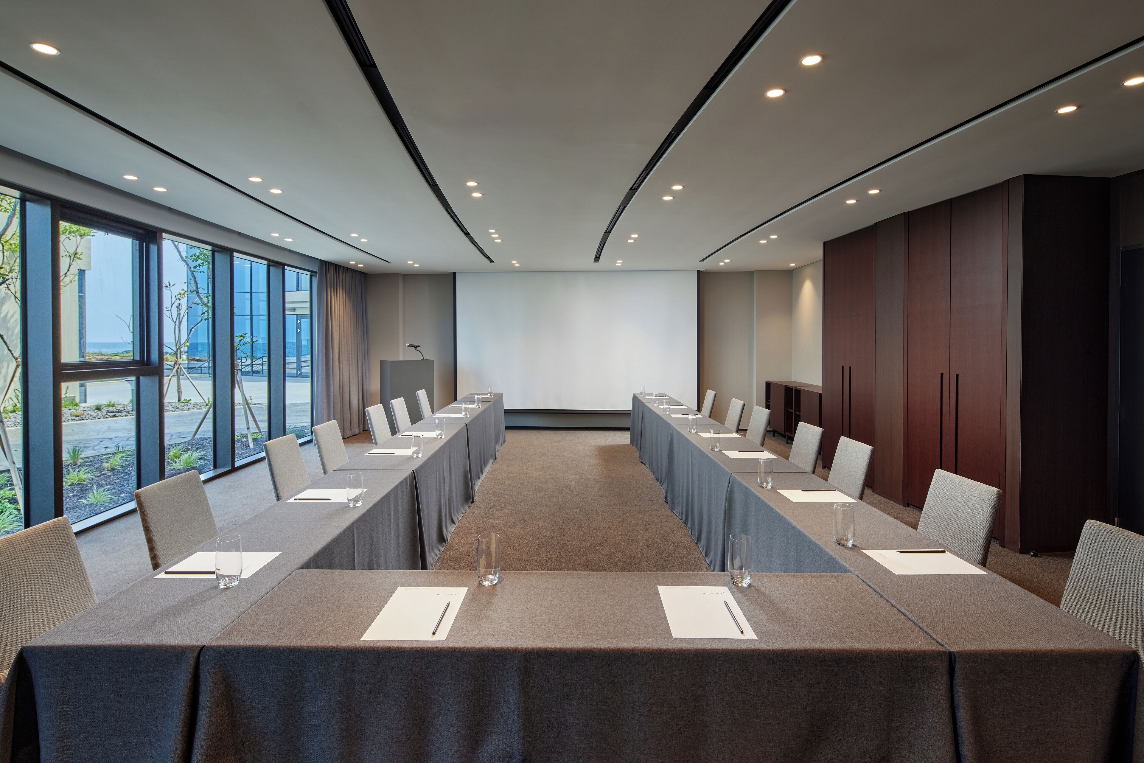 A conference room with a long table, chairs, and a projector screen.