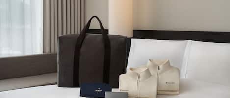 A bed with a grey bag, two beige bags, and a blue box with text on a hotel room.