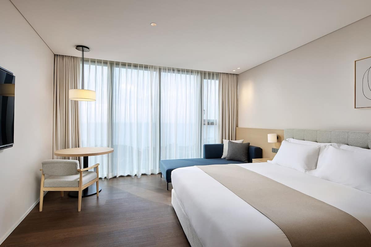 A hotel room with a large bed, a desk, a chair, and a TV.