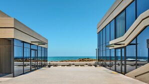 Un bâtiment moderne doté de grandes fenêtres en verre et d’une terrasse en bois donnant sur la plage.