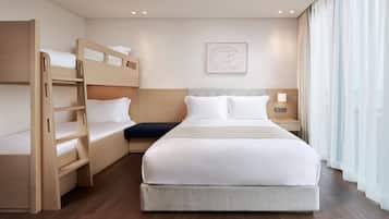 A hotel room with a bunk bed, a single bed, a bedside table with a lamp, a wall art piece, and a window with curtains.