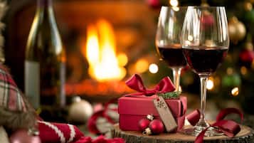 A cozy indoor setting with a fireplace, two glasses of red wine, a red gift box, and festive decorations.