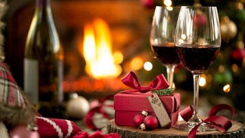 Ambiente interior acogedor con chimenea, dos copas de vino tinto, una caja de regalo roja y decoraciones festivas.