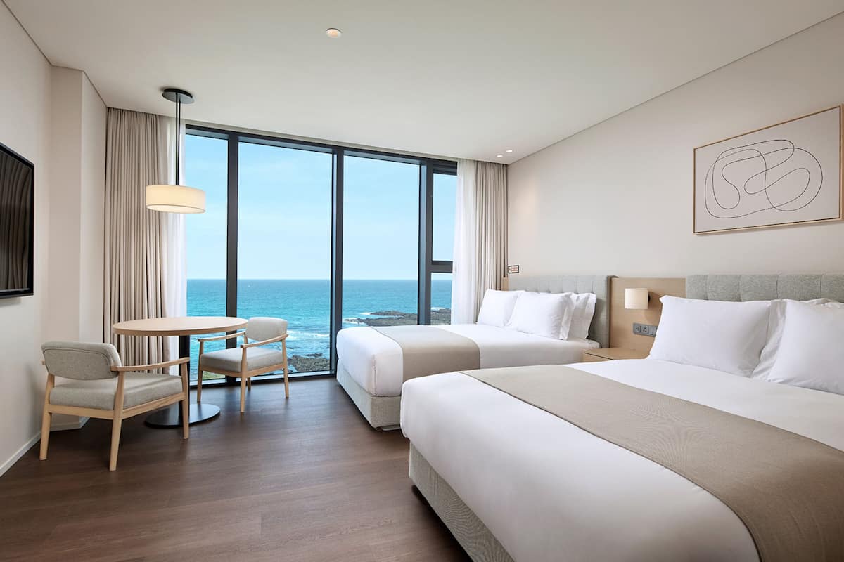 A hotel room with two beds, a dining table, and a view of the ocean.