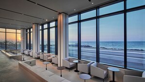 Un espace lounge moderne, doté de sièges et de tables, et de grandes fenêtres offrant une vue sur la mer.
